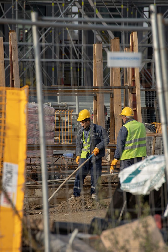 Home Two construction workers in safety gear collaborate efficiently in a busy construction site, emphasizing teamwork and hard work.