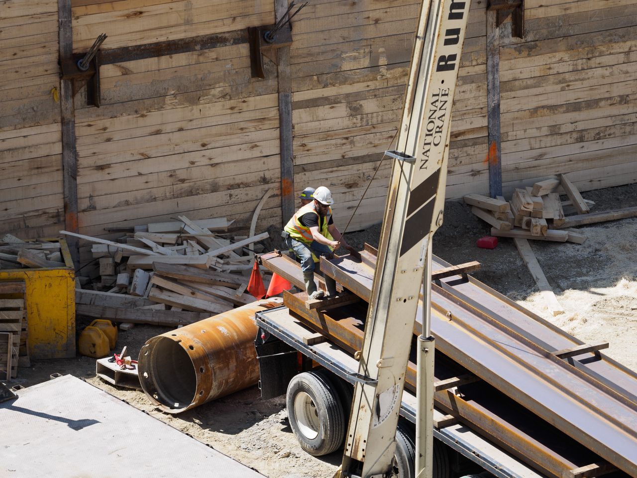 Construction workers maneuver steel beams at a busy urban job site.