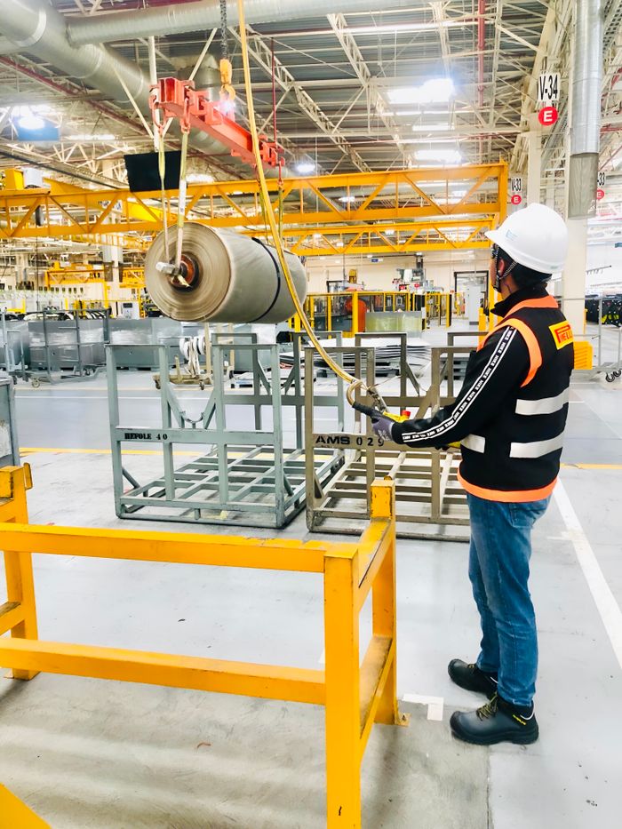 Home Worker operates a crane in a large industrial factory with safety gear.