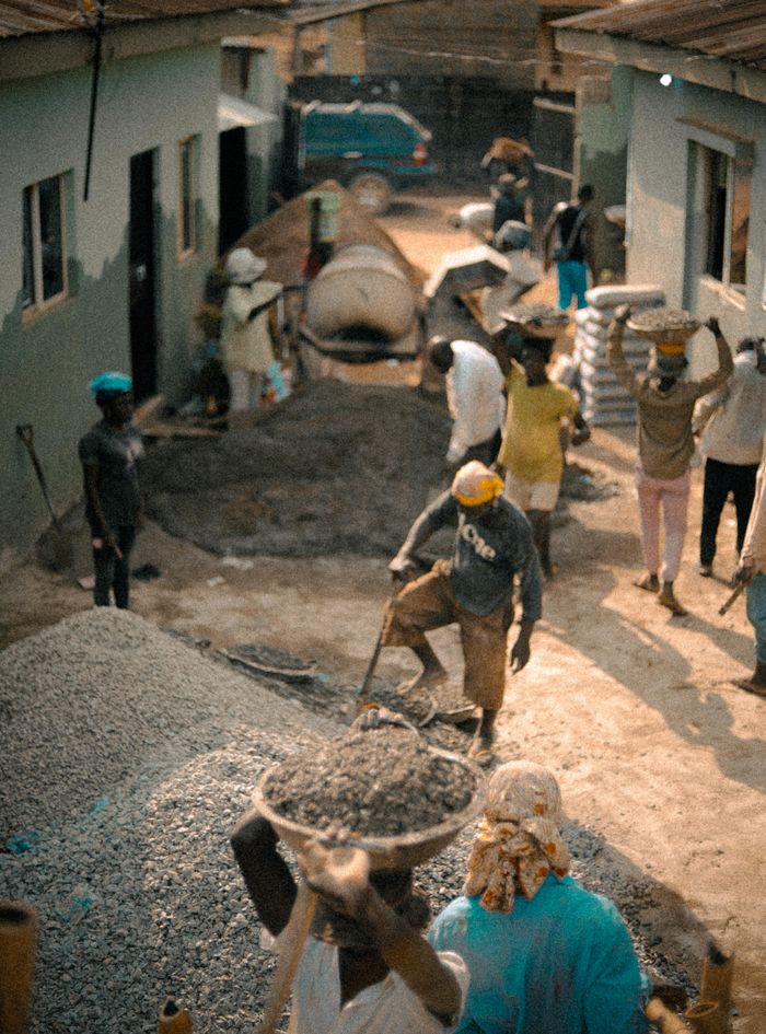 Aerial view of construction workers actively working on a site outdoors, carrying materials in bright sunlight.